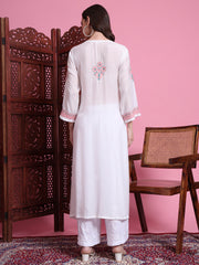Woman wearing a white kurta with pink embroidery in a room with pink walls and wooden furniture.