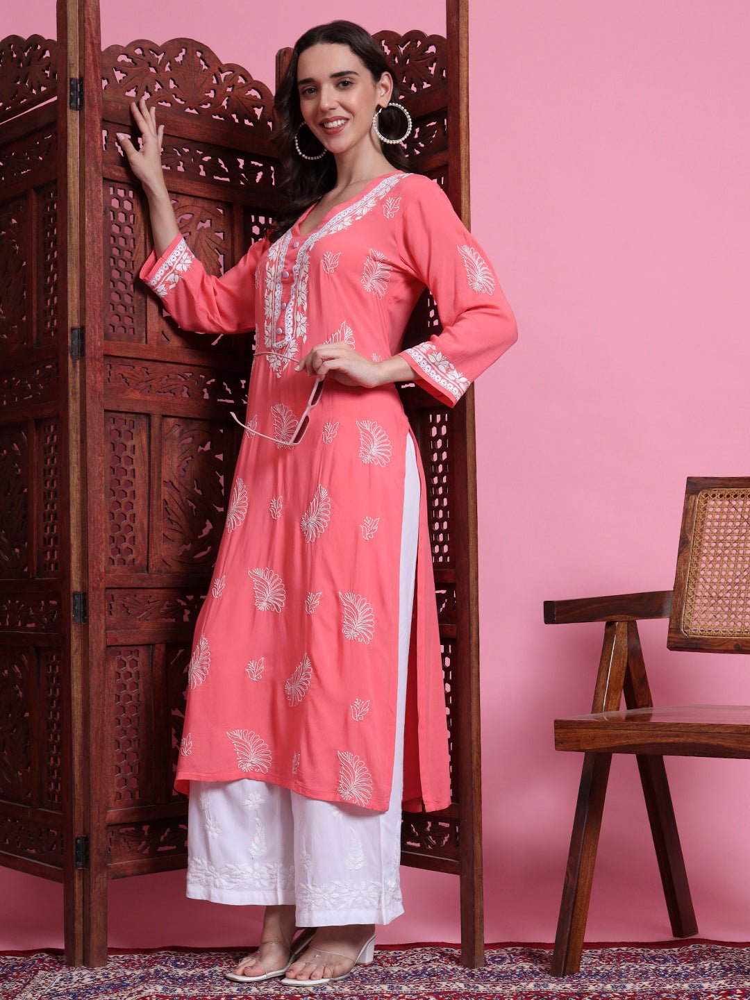 Woman in a pink and white traditional outfit standing against a pink wall.